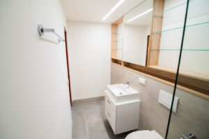 Compact bathroom with a white vanity cabinet, a mirror with glass shelves and a grey floor.