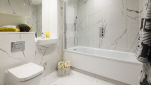 White bathroom with marble-effect tiles, a bath-shower screen and a wall-hung toilet.