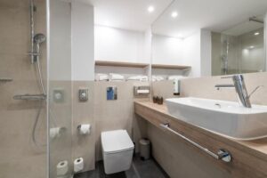 Bathroom with beige tiles, a walk-in shower, a wooden vanity with a countertop basin and a mirror.