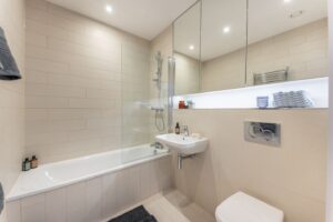 Beige bathroom with a bath-shower screen, a wall-hung toilet, a basin and a wall niche.