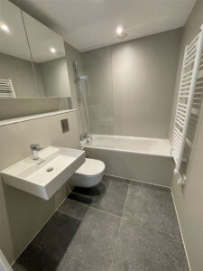 Grey bathroom with a bathtub and shower, a wall-hung toilet, a basin and a white towel radiator.