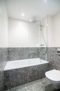 Bathroom with a bathtub and rain shower, finished in grey terrazzo, with a wall-hung toilet.