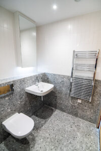 Grey terrazzo bathroom with a wall-mounted basin, a mirror cabinet and a chrome radiator.