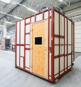 Prefabricated bathroom pod in production, with an OSB door panel and a window opening.