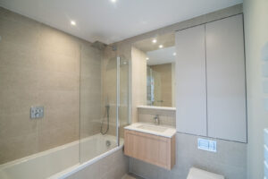 Bathroom with a bath-shower screen, beige tiles, a wooden vanity and a mirror cabinet.