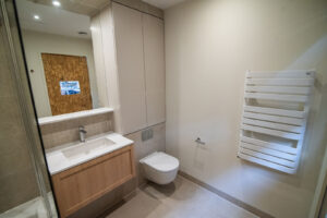 Bathroom with a wooden niche, a white vanity, a wall-hung toilet and a walk-in shower.