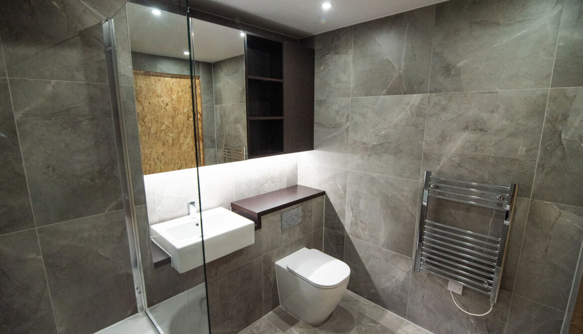 Grey bathroom with a bathtub behind a glass screen, a wall-hung toilet and a gold-accented niche.