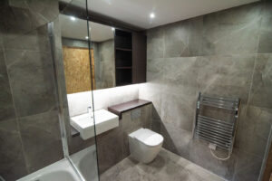 Grey bathroom with a bathtub behind a glass screen, a wall-hung toilet and a gold-accented niche.