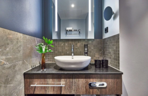 Bathroom with a countertop basin on a wooden vanity, a large mirror and a mosaic wall.