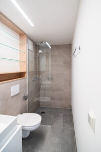 Narrow grey bathroom with a walk-in shower and a wall-hung toilet.