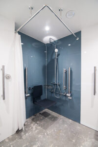 Barrier-free shower area with grab bars, a fold-down seat and a blue wall panel.