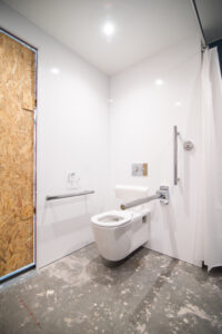 Barrier-free bathroom with a wall-hung toilet, grab bars for people with disabilities and an OSB door.
