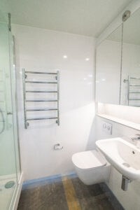 White bathroom with a shower enclosure, a wall-hung toilet, a basin and a chrome radiator.