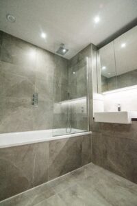 Grey bathroom with a bath and shower, a mirror cabinet and stone-effect tiles.