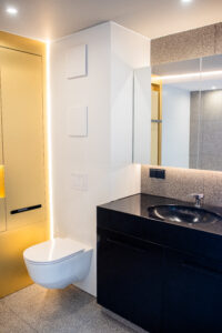 Bathroom with a yellow niche, a black vanity and a wall-hung toilet on a terrazzo floor.