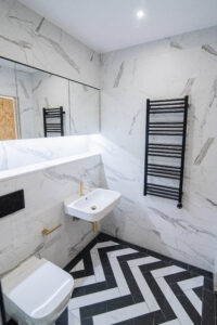 Elegant bathroom with marble-effect tiles, a black radiator and a black-and-white chevron floor.