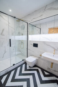Bathroom with marble-effect tiles, a glazed walk-in shower, gold accents and a chevron floor.