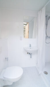 White bathroom with a curtained shower, a wall-mounted basin and a wall-hung toilet.