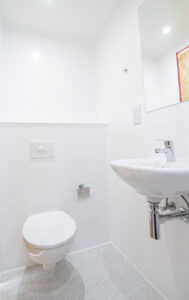 White bathroom with a wall-hung toilet, a wall-mounted basin and a mirror.