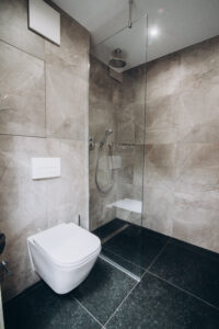 Grey bathroom with a walk-in shower with a seat, a wall-hung toilet and a dark floor.