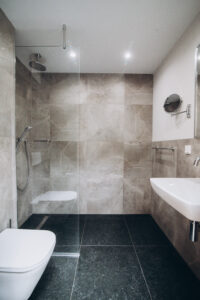 Grey bathroom with a walk-in shower, a wall-hung toilet, a basin and a dark floor.