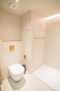 Minimalist beige bathroom with a wall-hung toilet and a walk-in shower.