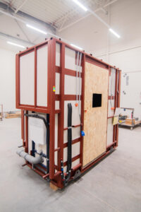Prefabricated bathroom pod on a red frame with an OSB door and plumbing.
