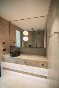 Bathroom with beige tiles, a stone vanity with a black countertop basin, a large mirror and a walk-in shower.
