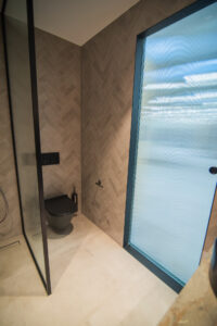Bathroom with herringbone tiles, a black shower glass partition and a black wall-hung toilet.