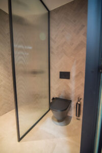 Bathroom with herringbone tiles, a black shower partition and a black wall-hung toilet.