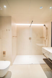 Beige bathroom with a walk-in shower, a wall-hung toilet, a basin and LED lighting.