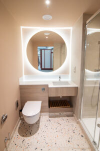 Bathroom with a round backlit mirror, a wooden vanity, a terrazzo floor and a walk-in shower.