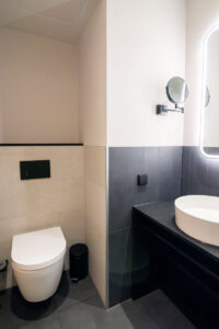 Two-tone bathroom with a black vanity, a round mirror and a wall-hung toilet.