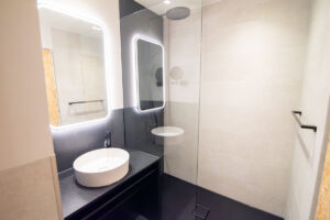 Bathroom with backlit mirrors, a countertop basin on a black vanity and a walk-in shower.