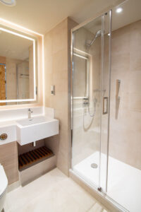 Beige bathroom with a backlit mirror, a basin and a shower enclosure.