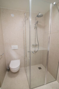 Beige bathroom with a walk-in shower with a rain head and a wall-hung toilet.